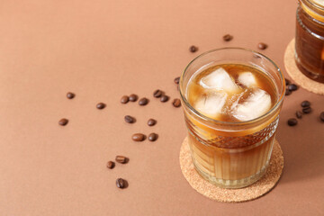 Glasses of ice coffee with beans on beige background