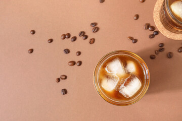 Glasses of ice coffee with beans on beige background