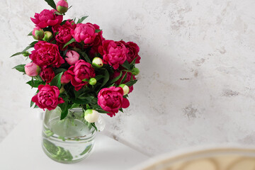 Vase with red peonies near beige grunge wall