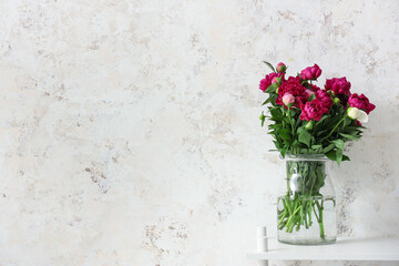 Fototapeta na wymiar Vase with red peonies near beige grunge wall