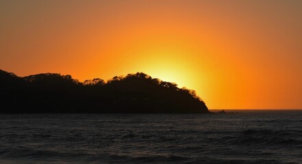 Fototapeta na wymiar Silhouette of an island against the glowing sun in the sunset sky