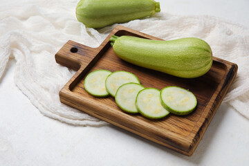 Wooden board with cut and whole zucchini on light background