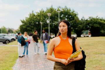 asian girl, young student, walks thoughtfully listening to music on the outskirts of the university...