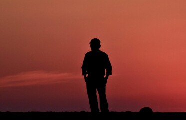 Fototapeta na wymiar Silhouette of a man standing with against the sunset sky with his hands in his pocket