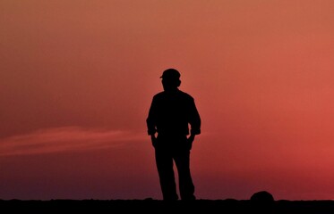 Fototapeta premium Silhouette of a man standing with against the sunset sky with his hands in his pocket