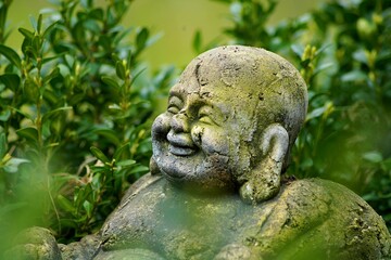 Closeup shot of smiling buddha statue with green plants in the background