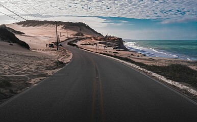 Fototapeta premium Highway road in arid landscape near the sea under blue cloudy sky