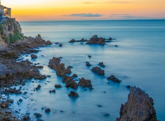 Aerial shot of pieces of sharp rocks in the quiet sea under the golden sky at sunset