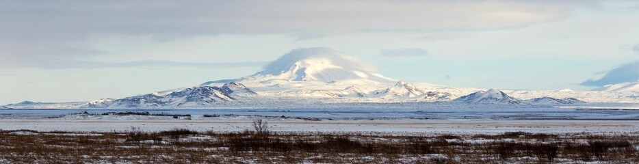 Obraz premium Panoramic shot of a mountain covered with snow under the blue sky and clouds