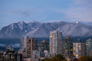 Scenic view of modern buildings against a mountain range covered with clouds in twilight