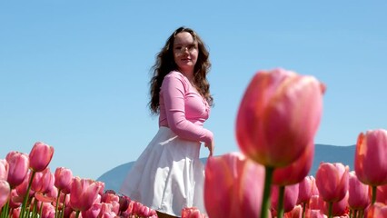 girl in white skirt walks through a field tulips dance spinning run touch flowers with her hands straighten hair on blue background sky mountains