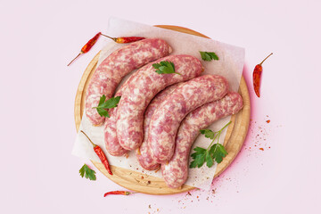 Board with raw fresh sausages and spices on pink background