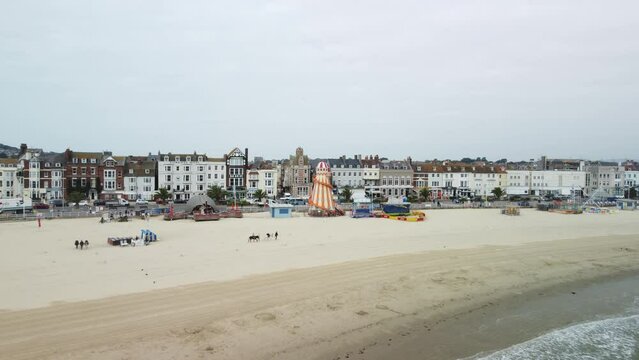 Drone shot of a man walking with two donkeys on the beach and playground with buildings row