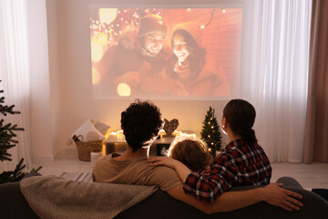Family watching Christmas movie via video projector at home, back view - obrazy, fototapety, plakaty