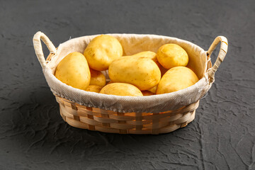 Wicker basket with raw baby potatoes on black background