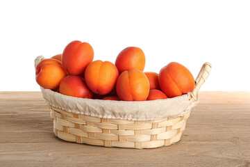 Wicker basket with ripe apricots on table against white background