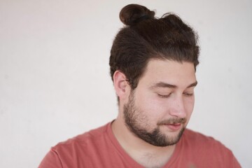 Fototapeta premium Closeup shot of a man with a ponytail hair looking away on the empty white background