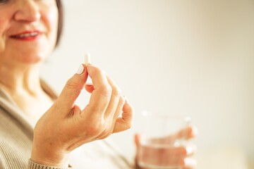 Fototapeta premium Close up of a retired woman in casual clothes at home holding pill and glass water. 
