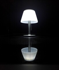 Vertical shot of a table lamp with reflection on mirror surface isolated on black background