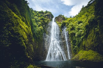 Scenic shot of waterfalls flowing to a lake surrounded bu lush greenery