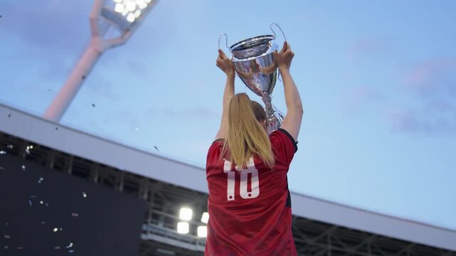 Portrait of Caucasian female soccer football player celebrating victory in the championship, lifting the trophy above her head in a huge stadium. Super slow motion, shot on RED cinema camera