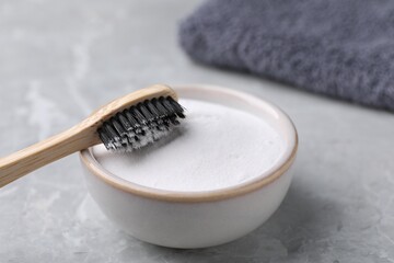 Bamboo toothbrush and bowl of baking soda on light grey table, closeup