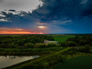 Aerial shot of a cloudy summer sunset over a railroad bridge and a green landscape
