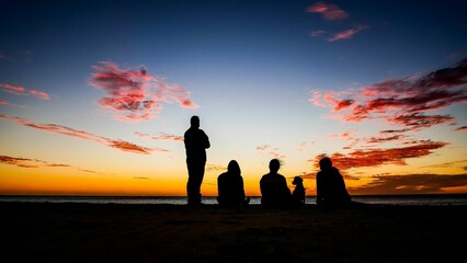 Silhouette of people watching vibrant sunset from the seashore