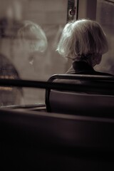 Vertical of an old woman sitting in a bus in London shot in grayscale