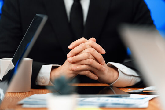 Closeup focus boss body language executive, CEO sitting confidently at meeting table or desk in professional harmony office workplace with hand clasped together, thinking and making business decision.