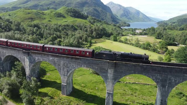 Drone view over train on Glenfinnan Viaduct railway over trees and Loch Shiel in Scotland