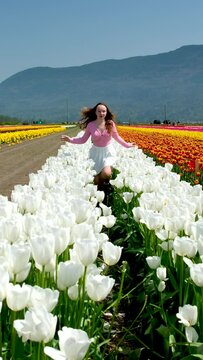 girl in white skirt walks through a field tulips dance spinning run touch flowers with her hands straighten hair on blue background sky mountains