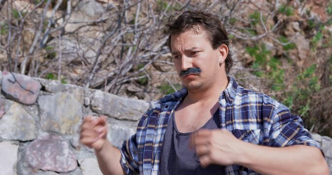 Man with mustache, village farmer in plaid shirt sits in park emotionally justifies himself impulsively waving his arms, argues. Street vendor traded, hand gestures. Offended husband justifies himself