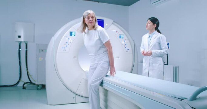 Middle-aged woman is going to MRI capsule. Female doctor is welcoming patient and explaining to patient how to lie down. Doctor and patient are getting ready for magnetic resonance imaging.
