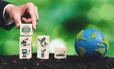Businessman hand holding wooden cube with eco symbol and paper globe on fertile soil background....