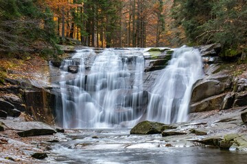 Fototapeta na wymiar Long exposure shot of the splashing waves o the waterfall in the autumn forest