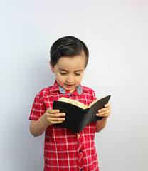 child reading the bible, head inclined forward, book, 5 year-old, red plaid shirt, straight black...