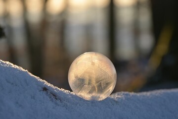 Fototapeta na wymiar Selective focus of a fragile frozen bubble, on a snowy ground, on a sunny day in winter