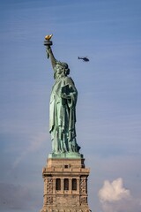 Statue of Liberty on a sunny day, with a helicopter flying in the blue sky in the background