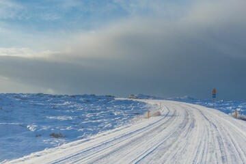Empty road covered in snow against a cloudy sky