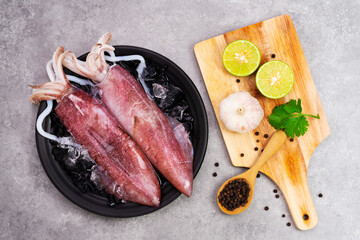 Fresh raw squid on a black plate with ice. Lemon slices. Top view and copy space for your text.