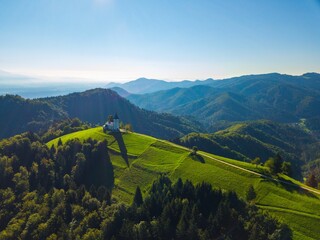 Aerial view of The Church of St. Primoz and Felicijan on top of lush green hill in Kranj, Slovenia