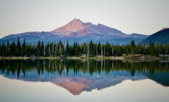 Scenic view of a lake reflecting green forests and mountains on its shore at sunset