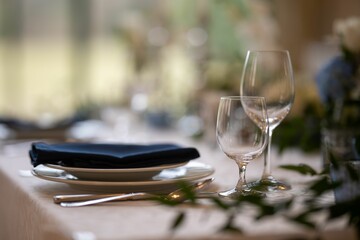 Closeup of a festive table with white dishes and glasses, blurred background