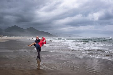 Man holding woman in his hands on the  beach. Middle age people having fun. Cannon beach. Portland....