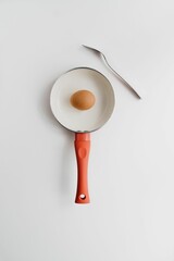 Vertical top view of whole raw egg in small cute pan on white background with copyspace