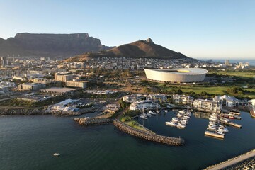 Naklejka premium Drone shot of white ships near wooden docks on the green-covered coast of a sea in Cape Town