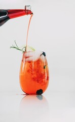 Vertical shot of soda water pouring into glass of spritz cocktail from a bottle