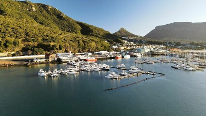 Fototapeta na wymiar Drone shot of white ships near wooden docks on the green-covered coast of a sea in Cape Town