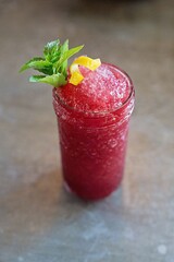 Vertical glass of an iced red fruit cocktail with lemon zest and mint